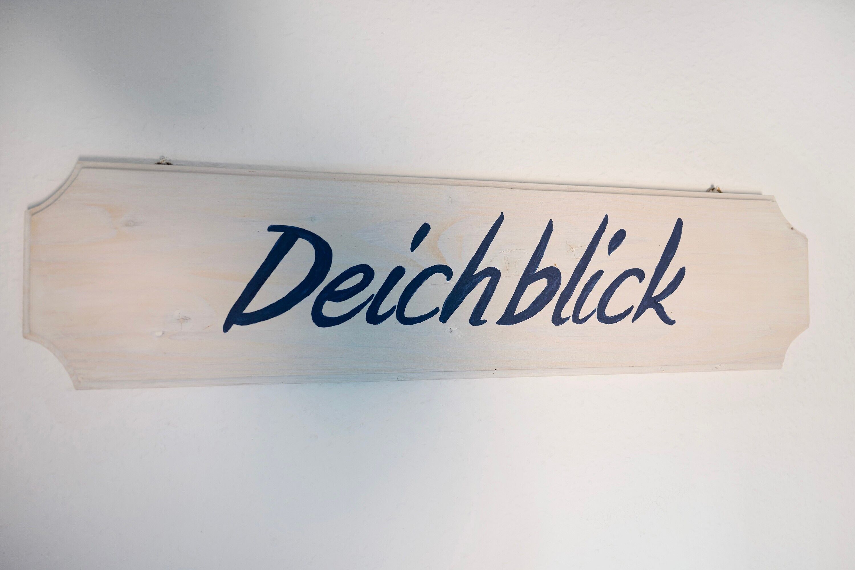 A wooden sign with the text 'Deichblick' mounted on a wall.