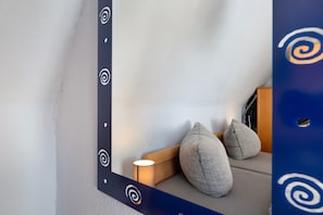 Um canto de um quarto com parede branca, um banco de madeira com almofadas e um espelho com design espiral.