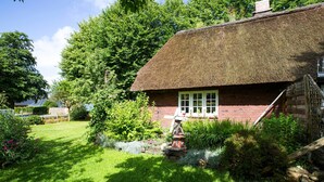 Ein reetgedecktes Häuschen mit Ziegelaußenwänden, umgeben von üppigem Grün und einem gepflegten Garten.