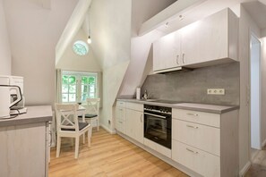 Uma cozinha com armários brancos, forno embutido e um espaço de refeições com cadeira e mesa.