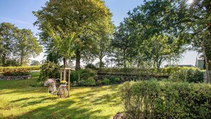 A garden with a bicycle, trees, and a stone wall. - Apartment 'Ferienwohnung Andresen Högel' with Shared Terrace, Shared Garden and Wi-Fi (Högel)