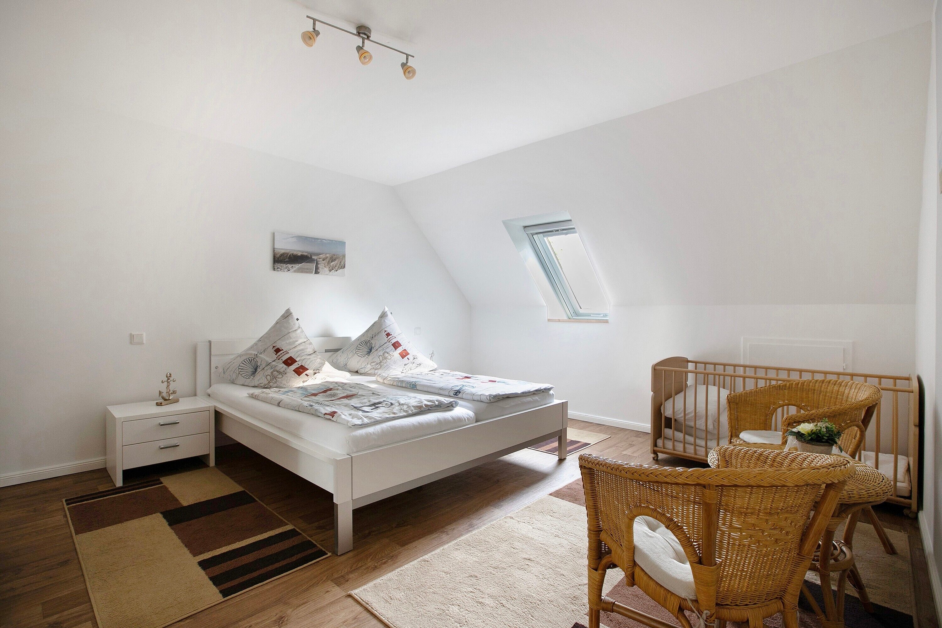 A bedroom with a bed, a nightstand, a crib, a window, and a ceiling light fixture.
