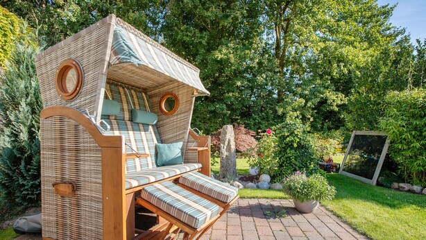 A wicker outdoor sofa with cushions and wheels, set on a paved area with greenery in the background. - Apartment 'Ferienwohnung Andresen Högel' with Shared Terrace, Shared Garden and Wi-Fi (Högel)