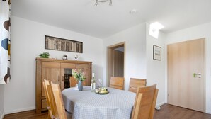 A dining area with a table set for two, wooden chairs, a cabinet, and a door. - Apartment 'Ferienwohnung Andresen Högel' with Shared Terrace, Shared Garden and Wi-Fi (Högel)