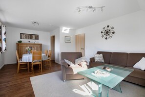 A living room with a sofa, a glass coffee table, a dining table with chairs, a cabinet, and a wall clock.
