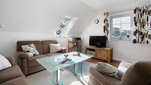 A modern living room with a glass coffee table, brown sofas, a TV, and a bookshelf. - Apartment 'Ferienwohnung Andresen Högel' with Shared Terrace, Shared Garden and Wi-Fi (Högel)