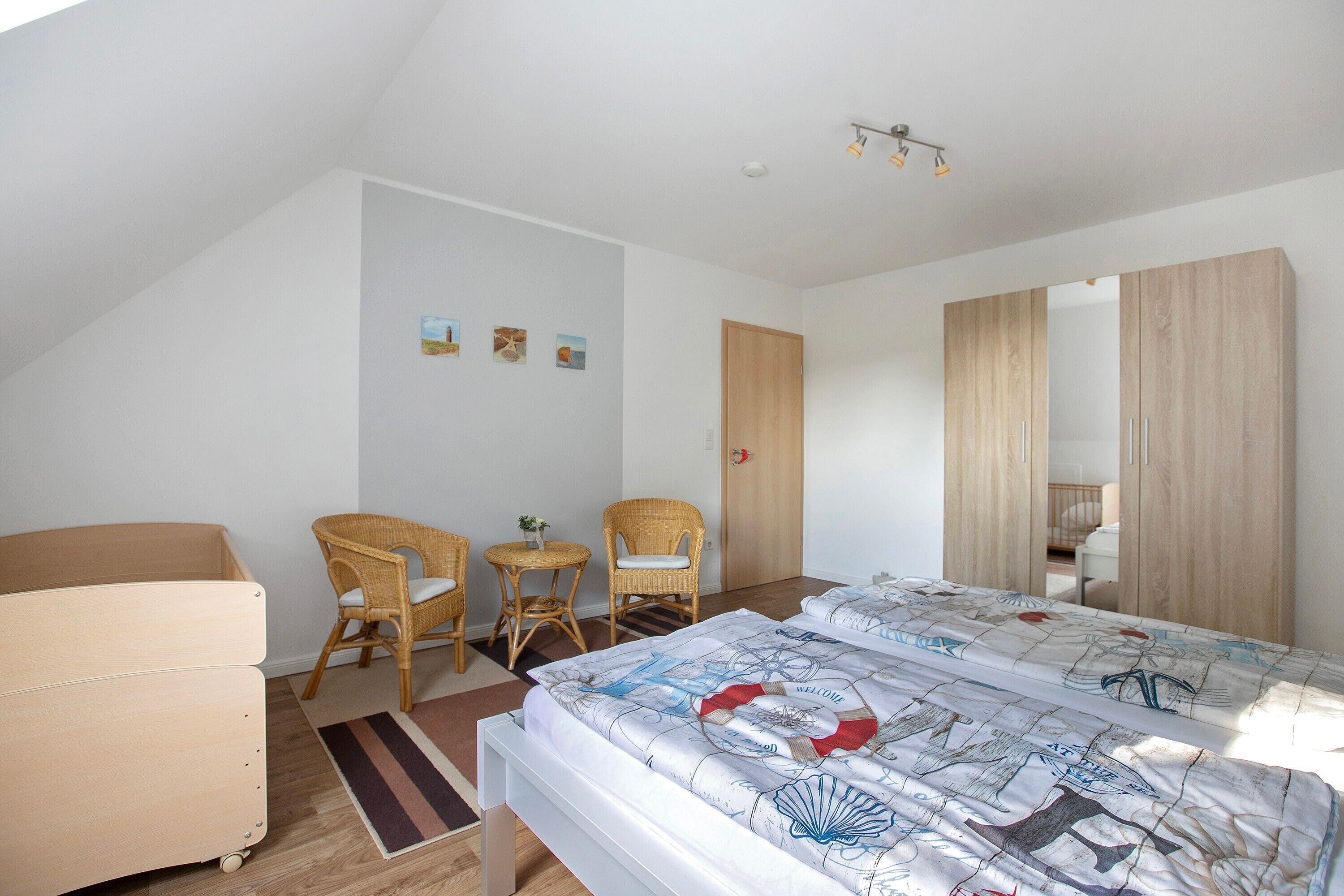 Un dormitorio con una cama, dos sillones de mimbre, una mesita, un armario de madera y una puerta.