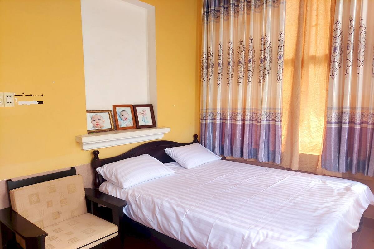 A neatly made bed with white linens, a wooden headboard, and a bedside table with a chair.