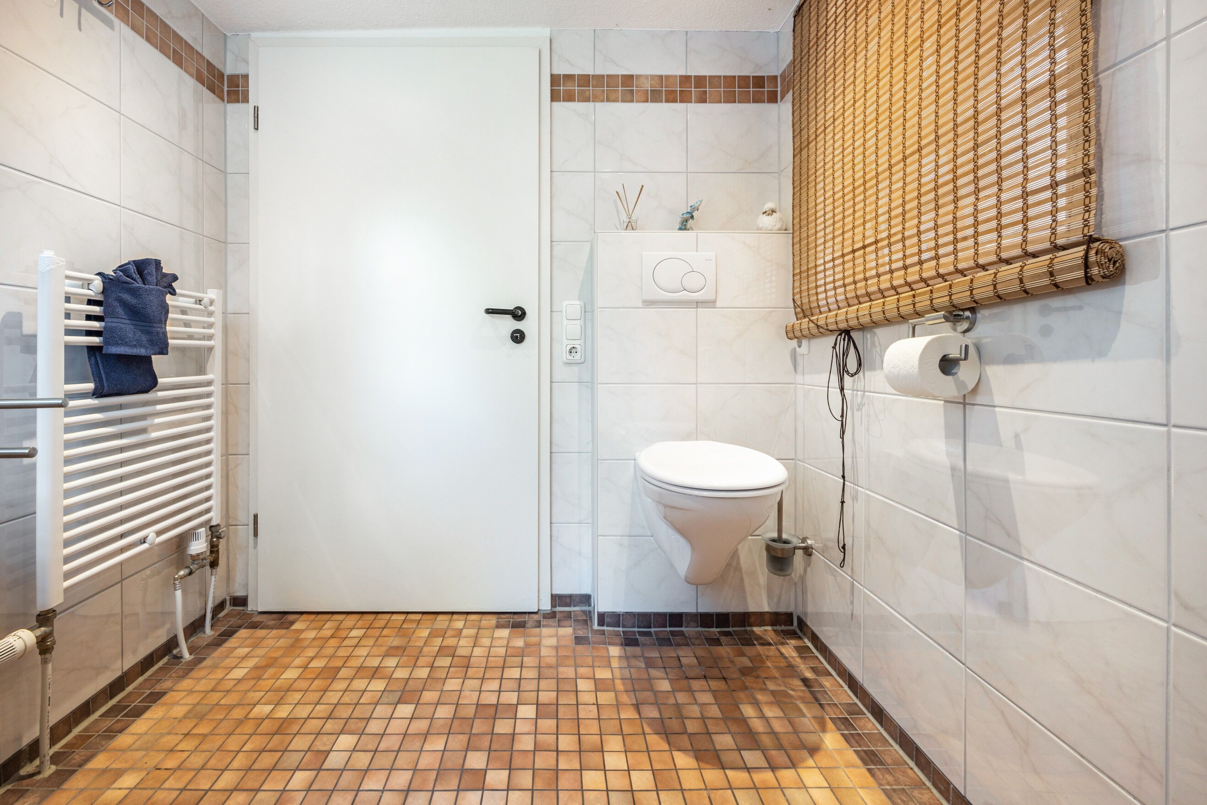 A bathroom with a white door, a toilet, a towel rack with a towel, a shower curtain, and a wall-mounted toilet paper holder.