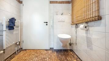 A bathroom with a white door, a toilet, a towel rack with a towel, a shower curtain, and a wall-mounted toilet paper holder.