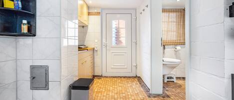 Un pasillo estrecho con suelo de baldosas, una puerta que da a un baño y un cubo de basura.