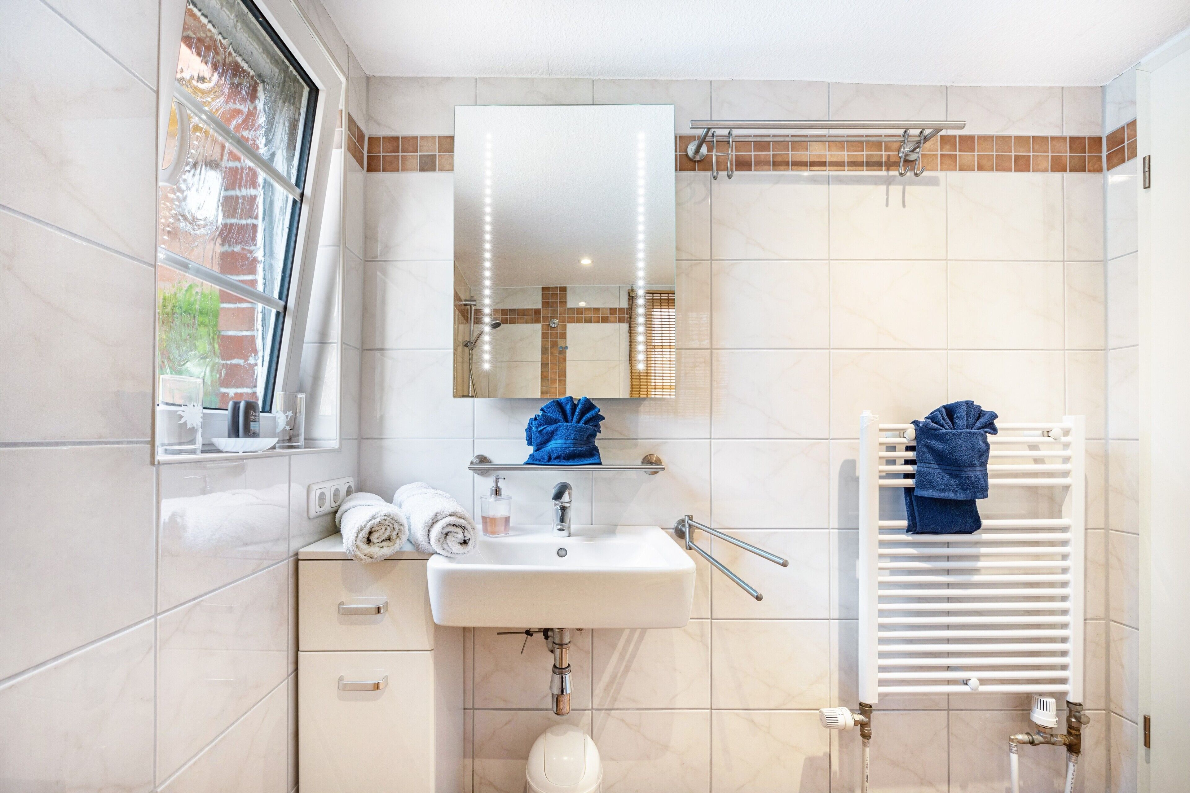 A bathroom with a sink, mirror, towel rack, and a window.