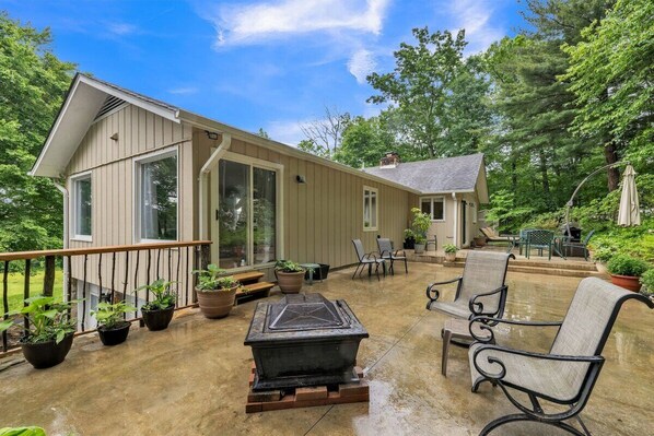 A covered patio with outdoor furniture, potted plants, and a stone fireplace.