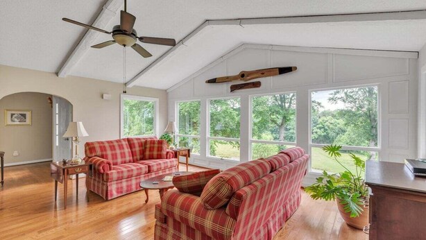 A spacious living room with a ceiling fan, large windows, a red plaid sofa, a wooden coffee table, and a potted plant. - Greene Hills Vista Cottage (Stanardsville)