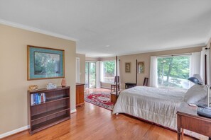 A bedroom with a bed, a bookshelf, a desk, and a window with a view of trees.