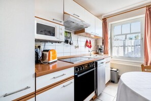 Une cuisine compacte équipée d’un four à micro-ondes, d’une cuisinière et d’un évier, de placards en bois et d’une fenêtre avec des rideaux.
