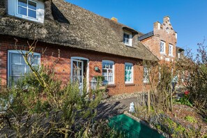 Une maison traditionnelle en briques, avec un toit de chaume, un petit jardin et une cheminée bien visible.