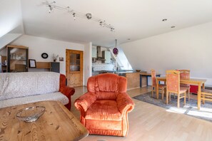 Un loft spacieux avec un plafond haut, un coin repas avec des meubles en bois et une cuisine à l’arrière-plan.