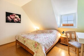 Une chambre à coucher avec un lit, un bureau, une chaise, un radiateur, une fenêtre et un tableau accroché au mur.