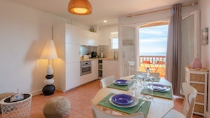 A modern kitchen with white cabinets, a dining area with a table set for two, and a balcony with a view. - Résidence Bellevue by Interhome (Les Issambres)