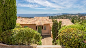 A traditional Mediterranean-style building with a tiled roof, surrounded by lush greenery and a view of the sea. - Résidence Bellevue by Interhome (Les Issambres)