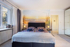 Une chambre avec un grand lit, une vue sur la mer par la fenêtre, un radiateur et une armoire.