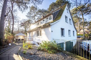 Une maison blanche avec un toit en pente, une terrasse couverte et une cour clôturée.