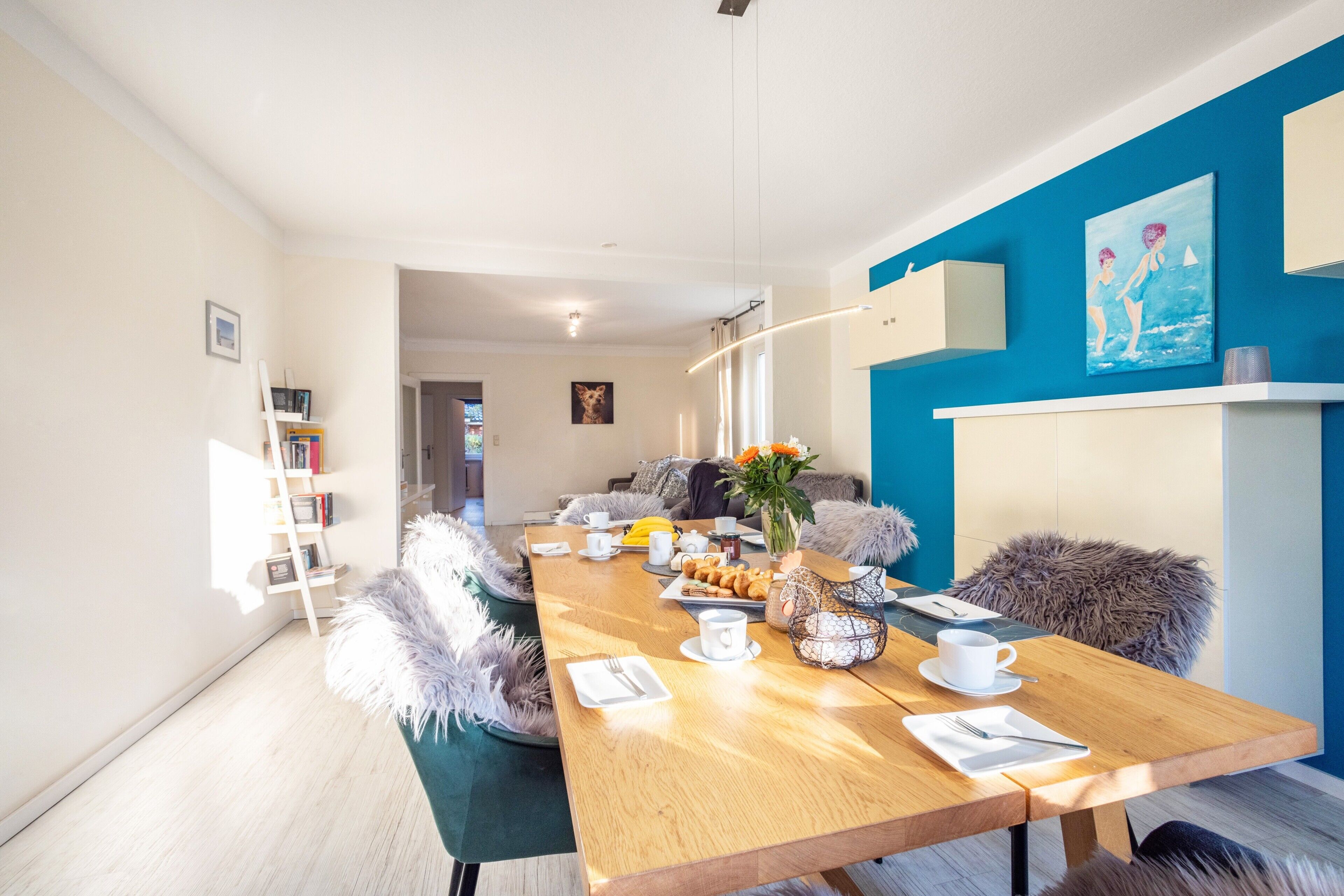 Ein moderner Essbereich mit einem Holztisch, der für das Frühstück gedeckt ist, einer blauen Akzentwand und Blick in einen anderen Raum.