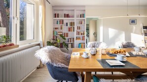 A cozy dining area with a wooden table, chairs, and a bookshelf filled with books. - Holiday Home 'Sandstrand' with Private Terrace, Garden, and Wi-Fi (Timmendorfer Strand)