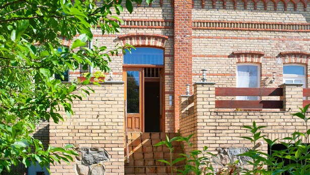 Un bâtiment en briques avec une porte en bois, des fenêtres en arc de cercle et des éléments décoratifs en pierre.