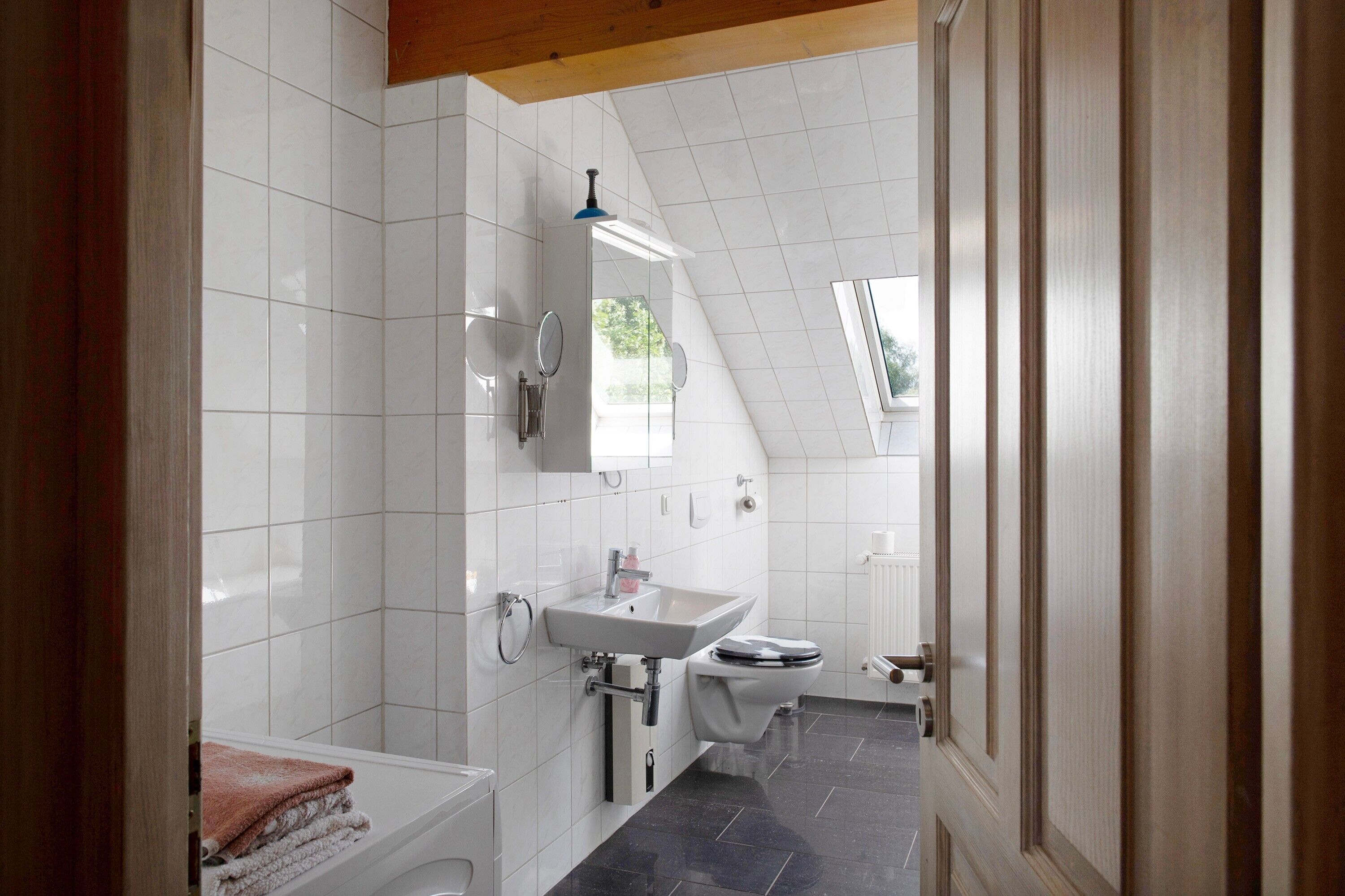 Ein modernes Badezimmer mit weißen Fliesen, einem Waschbecken, einer Toilette und einem Handtuchhalter.