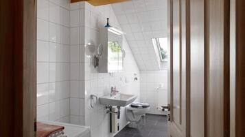 Ein modernes Badezimmer mit weißen Fliesen, einem Waschbecken, einer Toilette und einem Handtuchhalter.