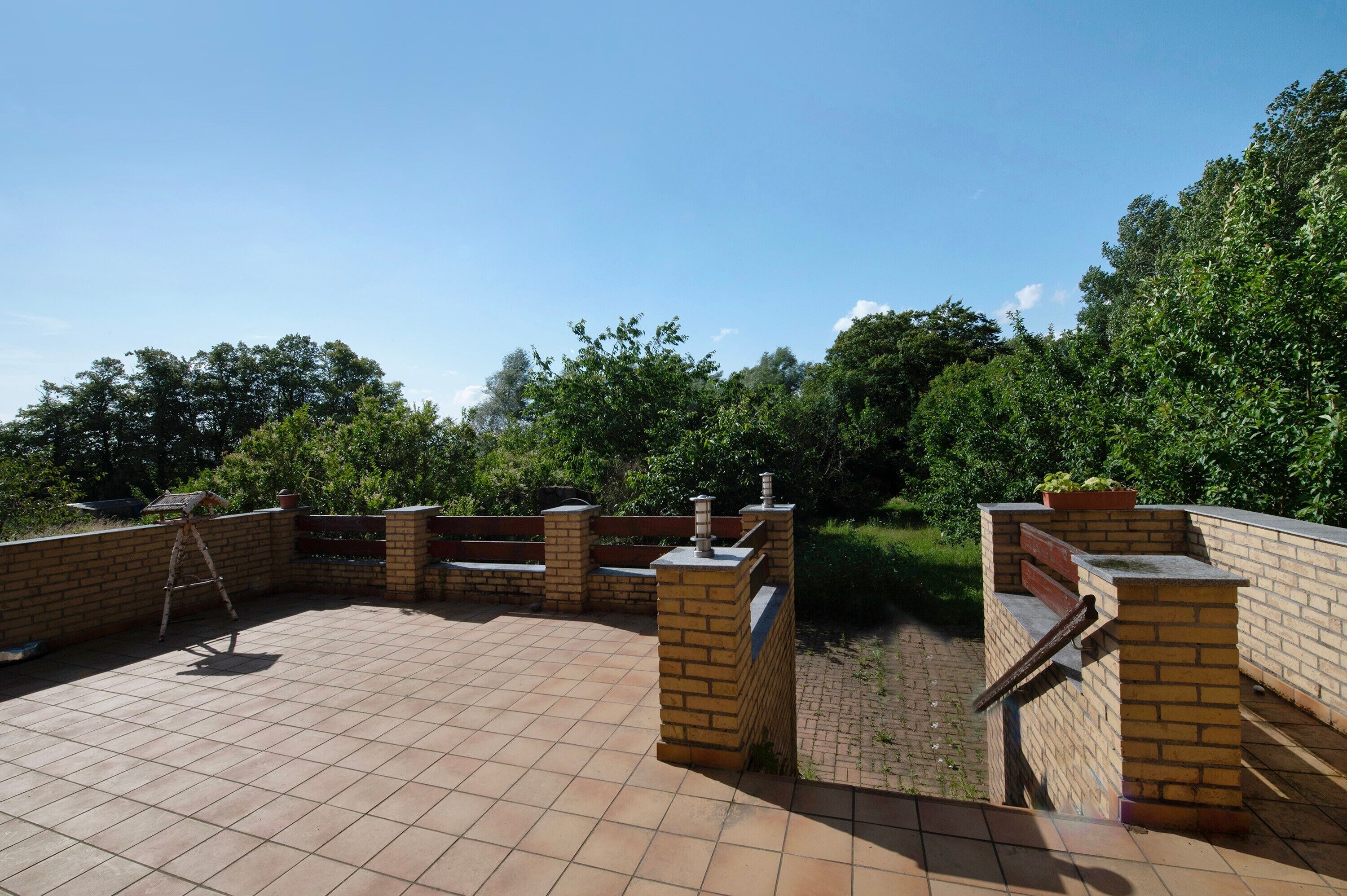 An outdoor patio area with a tiled floor, brick walls, and a wooden ladder.