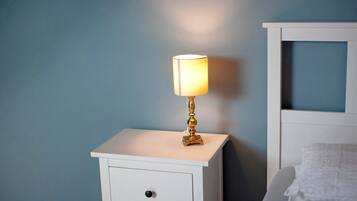 Ein weißer Nachttisch mit Lampe, einer Schublade und einem Bett mit weißem Kopfteil.