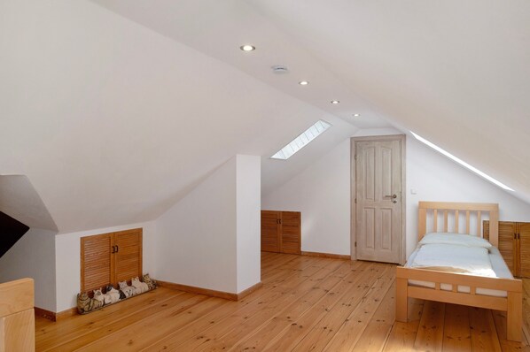 A bedroom with a sloped ceiling, wooden flooring, a bed, and a wardrobe.
