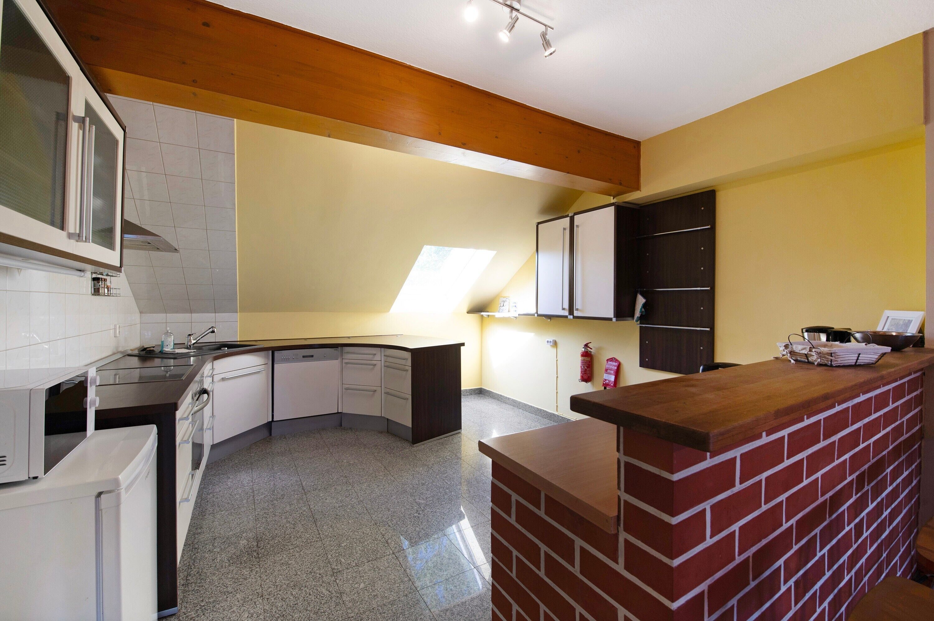 Una cucina con isola a penisola, elettrodomestici bianchi e soffitto in legno.