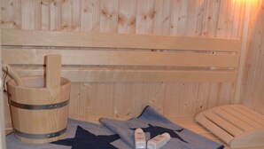 Una sauna de madera con un banco, un balde de madera, una toalla y una lámpara fijada a la pared.
