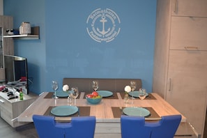 A dining area with a blue wall, a logo, a wooden table, blue chairs, and a bowl of fruit.