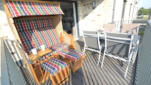 Una terraza con una silla y mesa de madera, un cojín a rayas y vistas a un edificio.