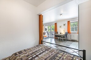 Une chambre à coucher avec un lit, une fenêtre avec des rideaux, une vue sur un coin repas et un radiateur.