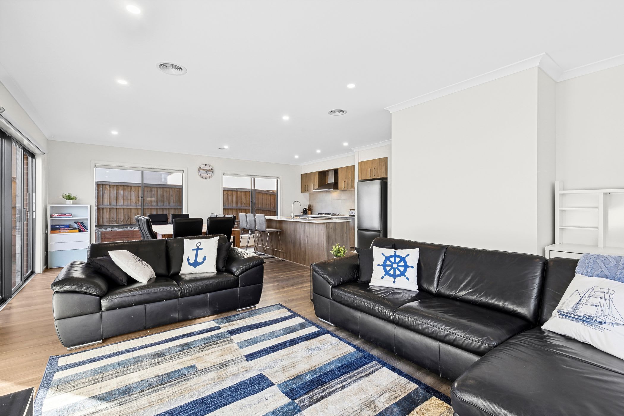 Ein modernes Wohnzimmer mit zwei schwarzen Ledersofas, einem Streifenmuster-Teppich und einer Küche im Hintergrund.
