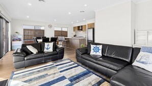 Un salon moderne avec deux canapés en cuir noir, un tapis à rayures et une cuisine en arrière-plan.