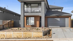 Une maison moderne à deux étages, dotée d’un balcon, d’un garage et d’un jardin paysager à l’avant.