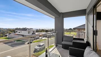 A balcony with a glass railing, a wicker sofa, and a table with a bottle and glass.