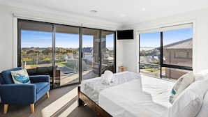 Une chambre d’hôtel moderne avec un grand lit, un fauteuil bleu et un balcon offrant une vue sur la ville.