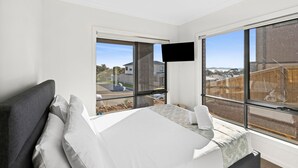 Une chambre moderne dotée d’un grand lit, d’un téléviseur à écran plat fixé au mur et de grandes fenêtres offrant une vue sur l’extérieur.