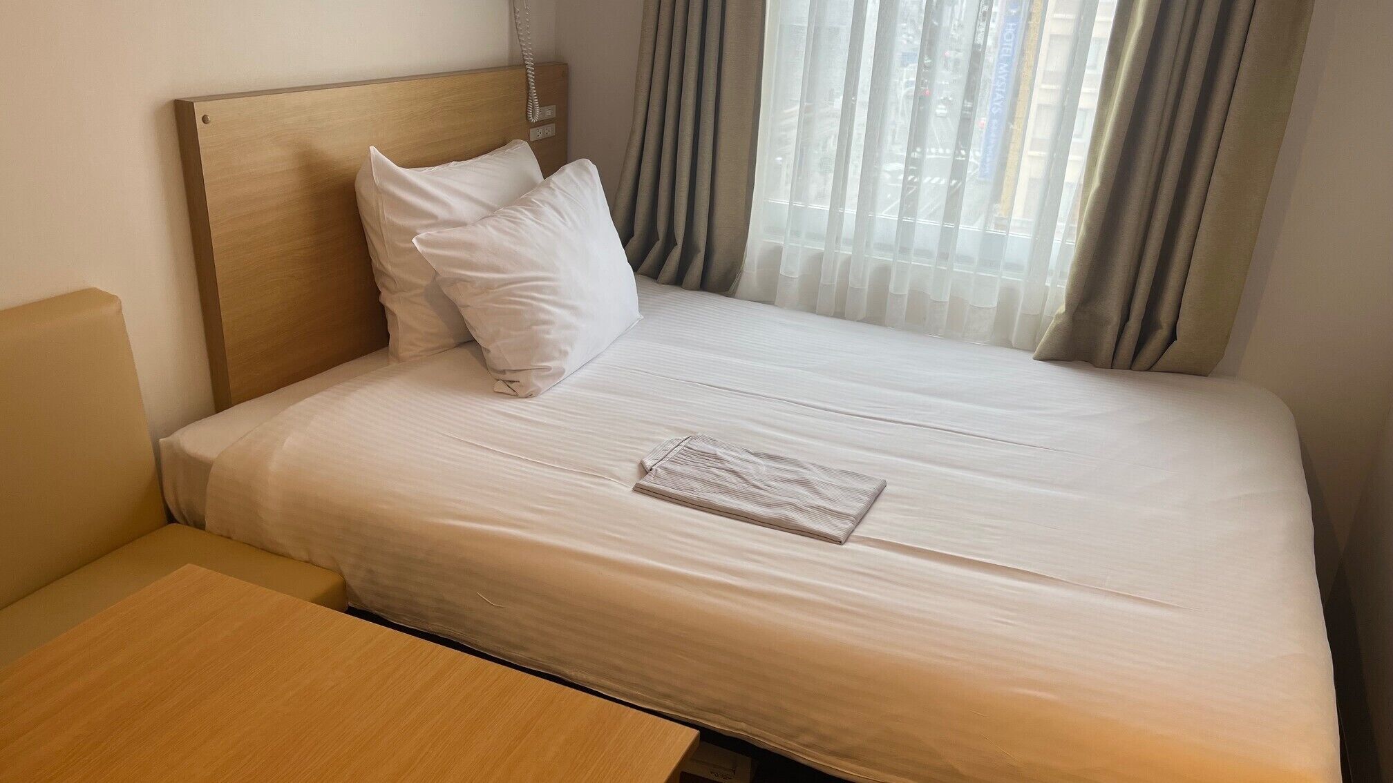A neatly made bed with white linens, a wooden headboard, and a small wooden table beside it.