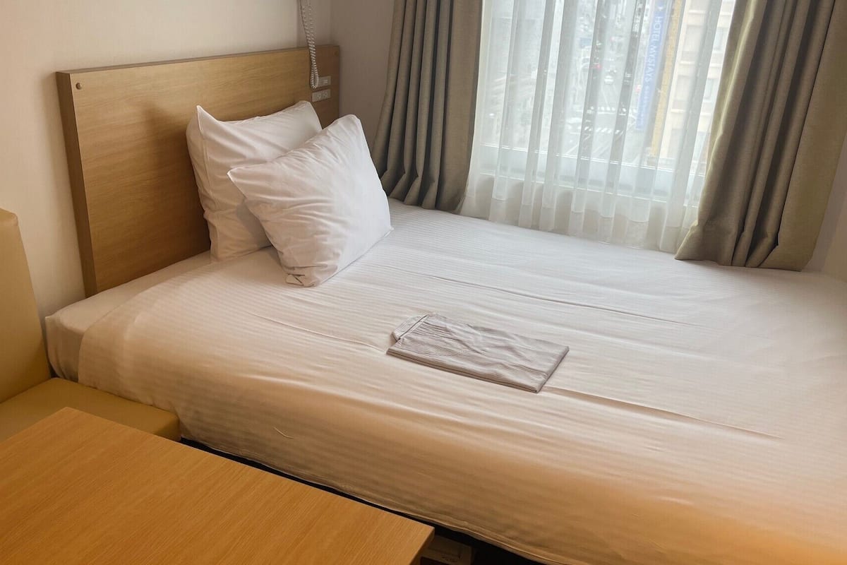 A neatly made bed with white linens, a wooden headboard, and a small wooden table beside it.