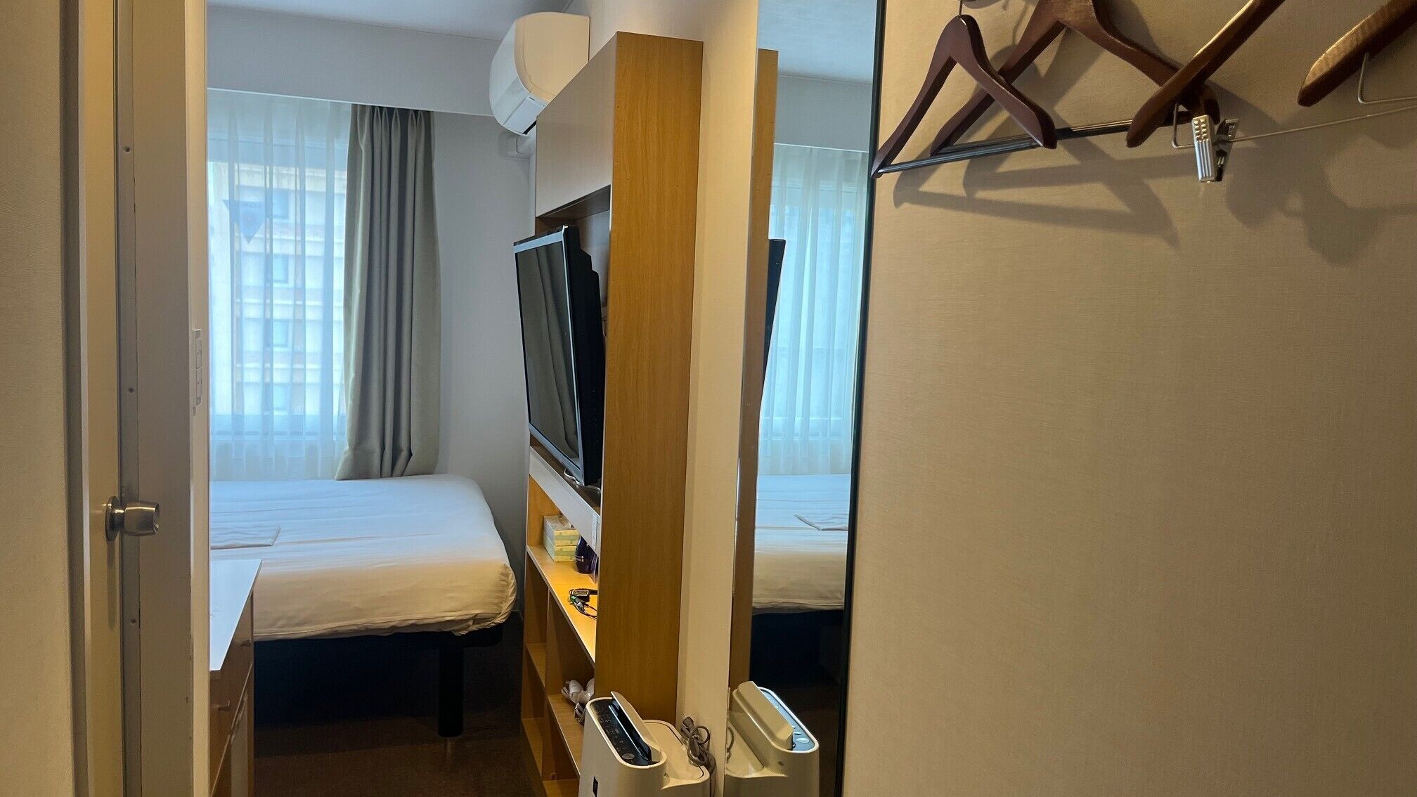 A hotel room with a bed, a TV, a desk with a phone, and a mirror.