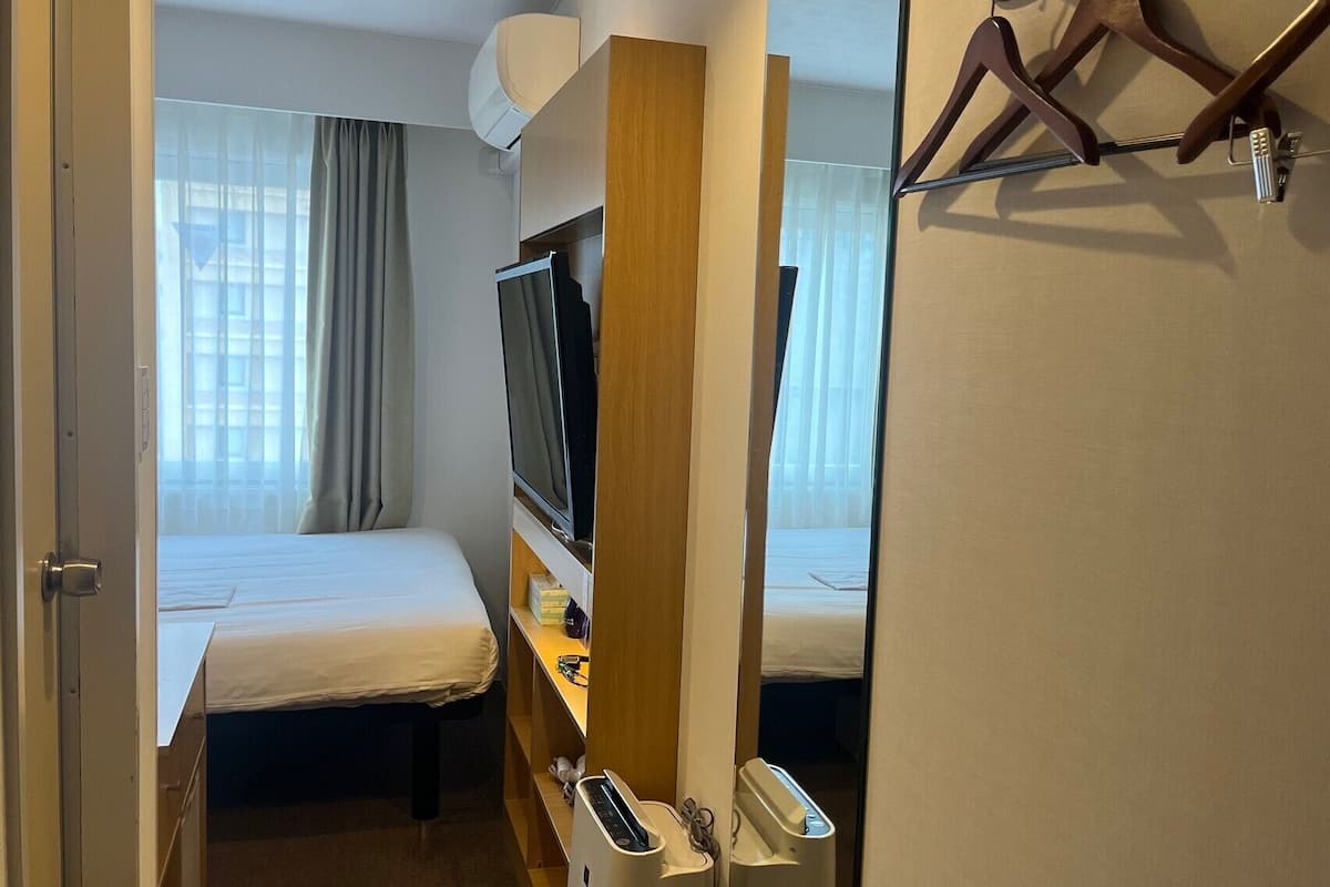 A hotel room with a bed, a TV, a desk with a phone, and a mirror.